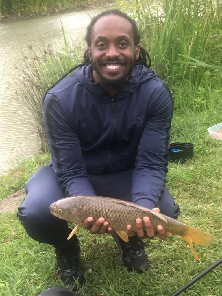 Fish-1-Optimised Angler kneeling with a common carp beside a fishing lake