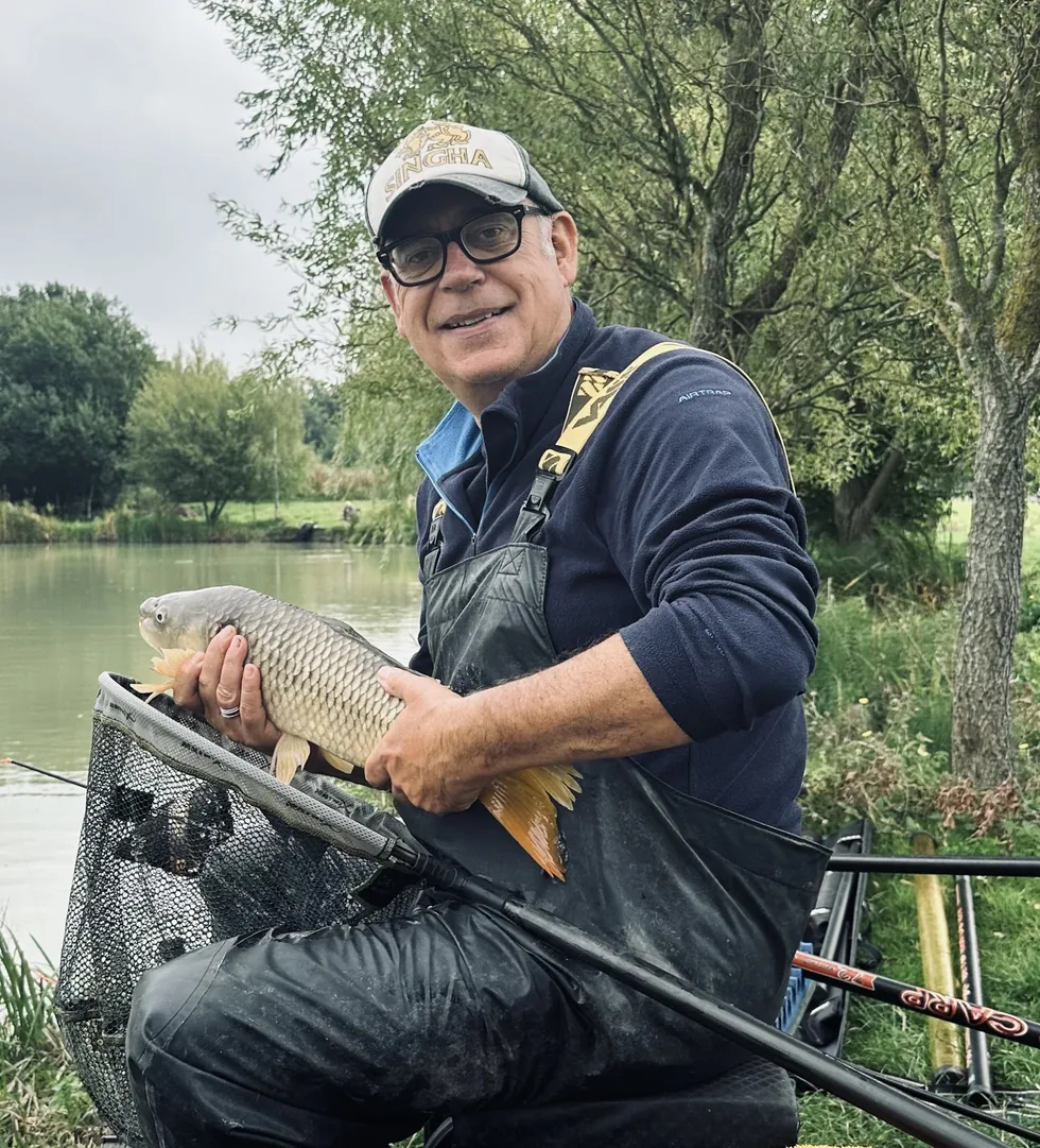 Fish-2-Optimised Angler holding a common carp beside a fishing lake