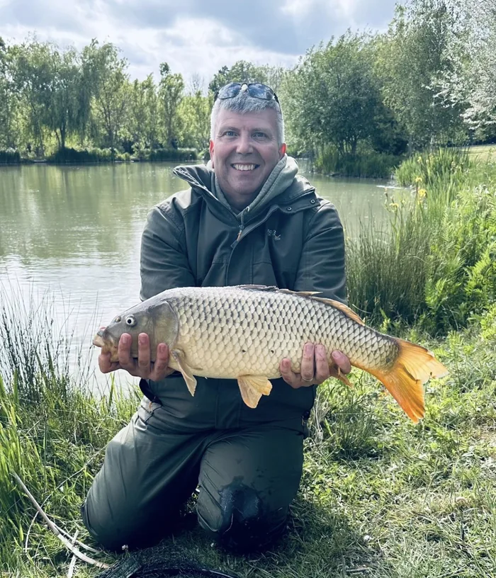 Fish-3-Optimised Angler holding a large common carp beside a fishing lake